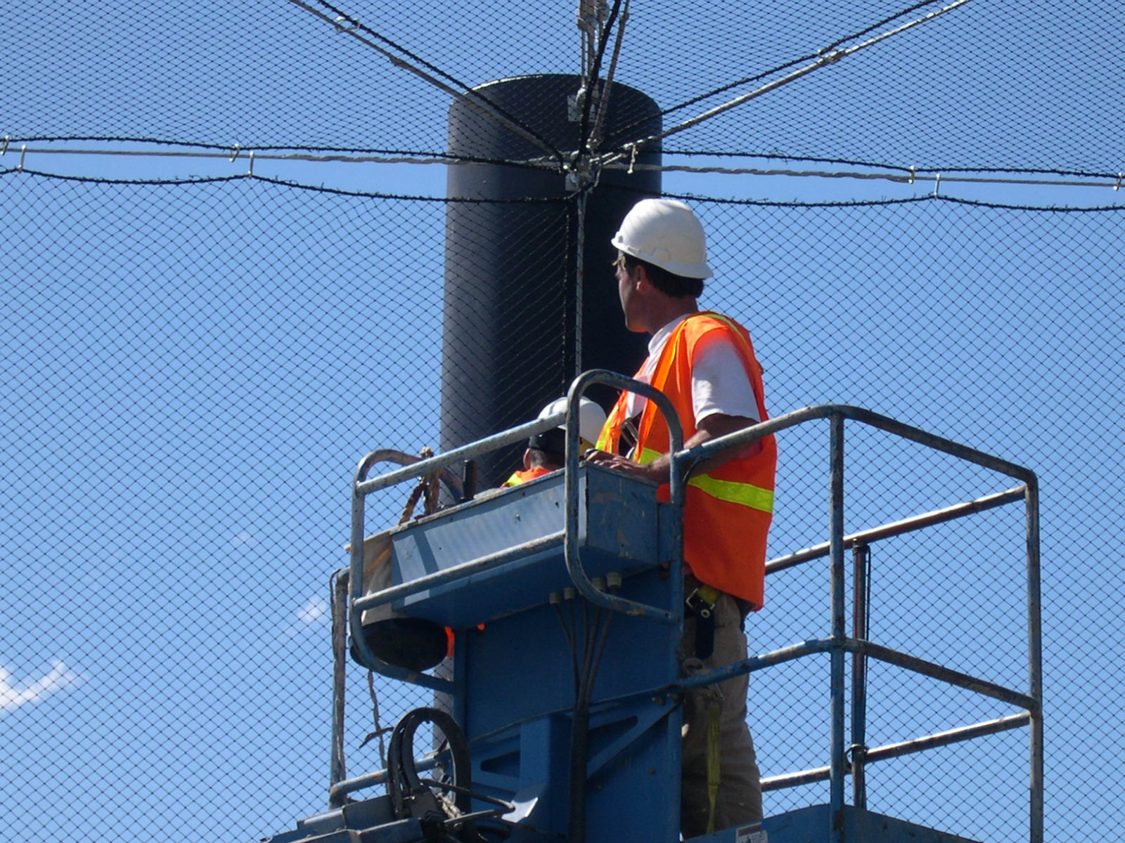 Worker installing outdoor netting and rope connections from a manlift